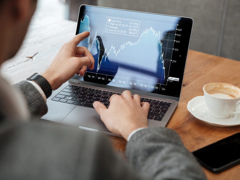 Cropped image of business man sitting by the table in cafe and analyzing indicators on laptop computer